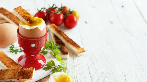  Huevo hervido con tostadas y tomates sobre una mesa de madera blanca
  - Foto, Imagen