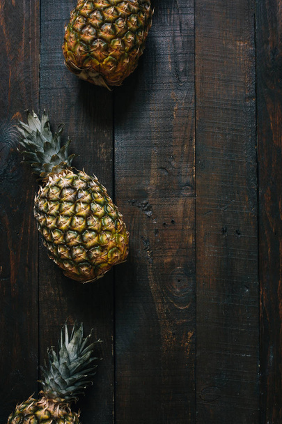 Ripe pineapples on dark wooden background. Tropical fruit creative concept. Empty space for copy, text, lettering. - 写真・画像