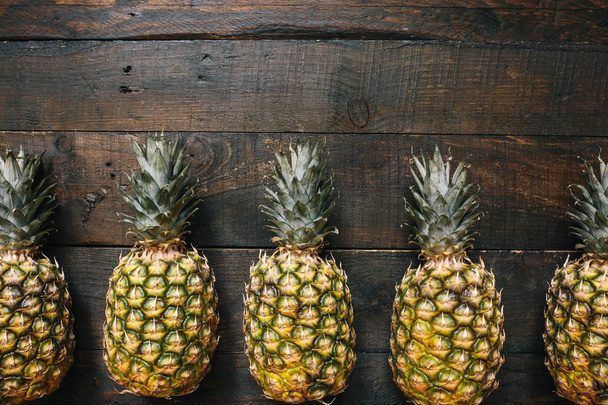 Ripe pineapples border frame on dark wooden background. Tropical fruit creative concept. Room for copy, text, lettering. - Foto, Imagem