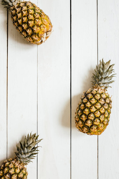 Ripe pineapples border frame on white wooden background. Tropical fruit creative concept. Room for copy, text, lettering. - Photo, Image