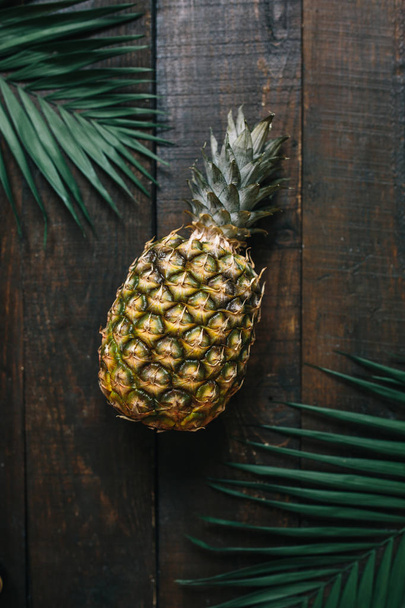 Ripe pineapple, palm leaves frame on dark wooden background. Tropical fruit creative concept. - Фото, изображение