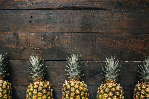 Ripe pineapples border frame on dark wooden background. Tropical fruit creative concept. Room for copy, text, lettering. - Fotó, kép