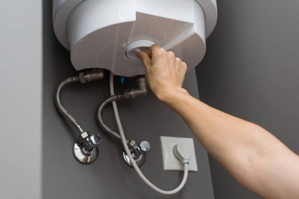 Woman hands setting temperature of water in heater electric boiler. Interior details close-up - Photo, Image