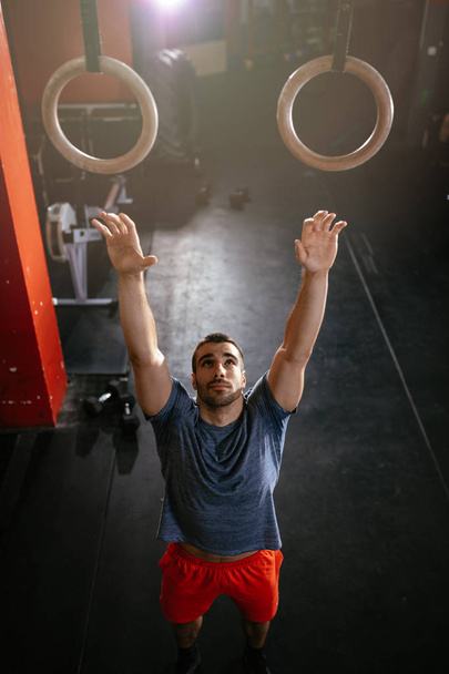 Młody człowiek mięśni robić ćwiczenia na pierścienie gimnastyczka siłowni - Zdjęcie, obraz