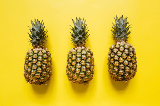Tree ripe pineapples on vivid yellow background isolated. Minimalist style trendy tropical concept. - Foto, afbeelding