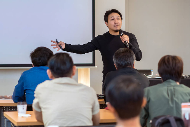 Азиатский спикер в повседневном костюме на сцене в низком свете на экране презентации в бизнес-семинаре или семинаре по образованию
 - Фото, изображение