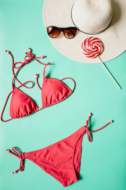 Traje de bikini rojo, rosa, piruleta, gafas de sol, sobre fondo cian claro. Espacio vacío para copiar, texto, letras. Concepto vacaciones de verano. Cartel vertical, banner, plantilla de postal
. - Foto, Imagen