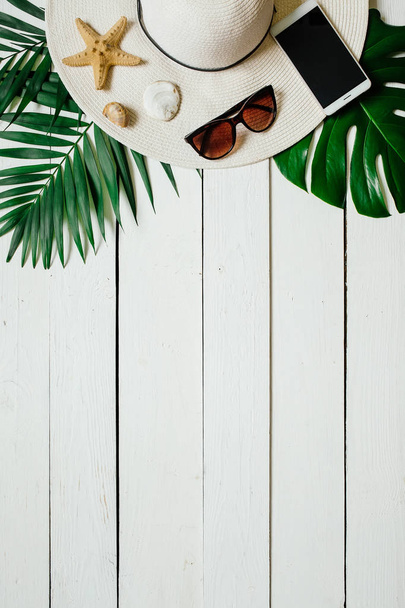 Chapeau, lunettes de soleil, smartphone, étoile de mer, feuilles de palourdes vertes disposées sur un sol en bois. Vacances d'été concept de vacances. Bannière d'affiche, modèle de carte postale
. - Photo, image