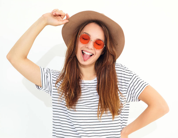 Portrait of young stylish laughing girl model in casual summer clothes in brown hat with natural makeup isolated on white background. Showing her tongue - Фото, изображение