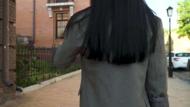 Long-haired brunette in grey coat walking at urban street - Video