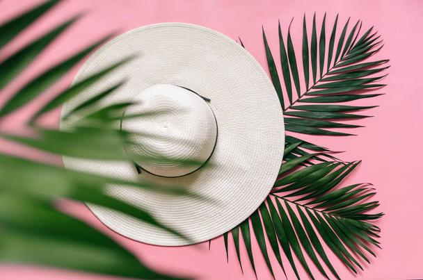 配置された光のピンクの背景にホワイト麦わら帽子と緑のヤシを残します。ミニマリスト スタイルの夏の休暇のコンセプトです。コピー、テキスト、レタリングの空スペース. - 写真・画像