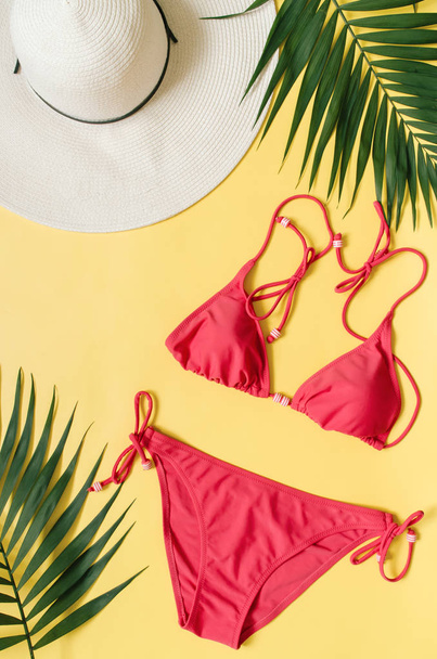 Beach kleding en tropische bladeren gerangschikt op gele achtergrond. Zomer vakantie minimalistische stijl concept. - Foto, afbeelding