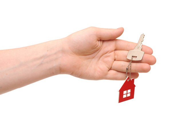 La mano que sostiene la llave con un llavero en la forma de la casa en th
 - Foto, Imagen