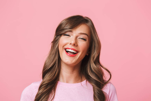 Image closeup of cheerful european woman 20s with long curly hairstyle and evening makeup laughing while looking at you with happy look isolated over pink background - Fotografie, Obrázek