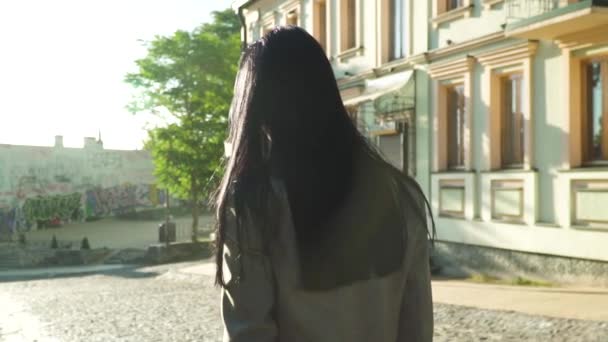 Stylish brunette in grey coat walking in sun rays at the street in slow motion - Кадри, відео