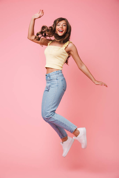Happy full length photo of cheerful woman with long brown hair rejoicing and jumping isolated over pink background - Φωτογραφία, εικόνα