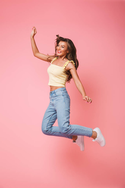 Happy full length photo of attractive brunette woman with long hair rejoicing and jumping isolated over pink background - Foto, imagen