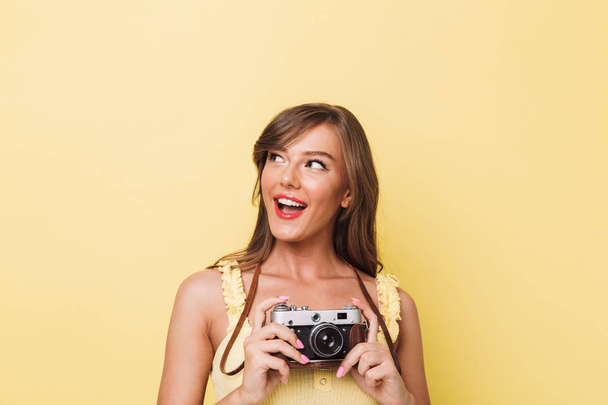Fotoğraf kamera tutarak ve sarı arka plan üzerinde izole kopya alanı bakarak mutlu bir genç kız portresi - Fotoğraf, Görsel