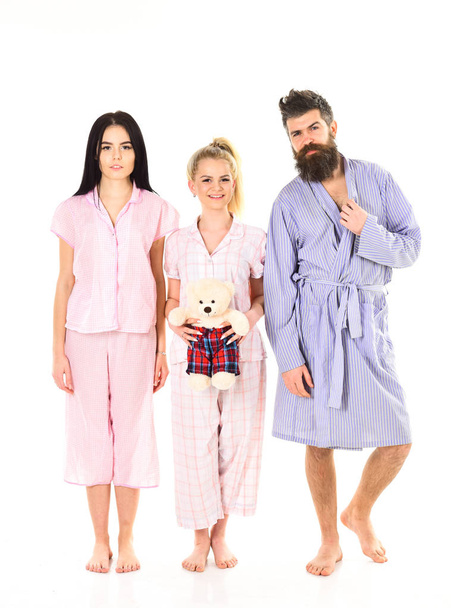 Girls with bearded macho in pajamas and robe in morning, isolated white background. Man with beard, cute blonde and brunette girls with toy bear just wake up in morning. Sleepy morning concept - Photo, Image