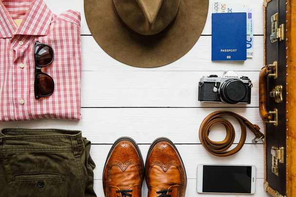 Vintage csípő ruhákat, kalapot, smartphone, tartozékok, bőrönd, a csomagolás előtt fehér fából készült asztal. Utazási koncepció. Üres hely másolás, szöveg, betűk. - Fotó, kép