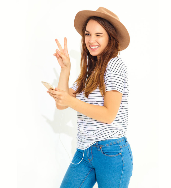 beautiful girl in casual hipster summer clothes with no makeup in brown hat listening music in smartphone with headphones isolated on white. Dancing - Φωτογραφία, εικόνα
