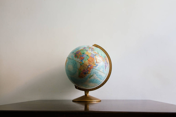 Globe model na ciemne drewniane biurko. Białe ściany pustej przestrzeni tła. - Zdjęcie, obraz