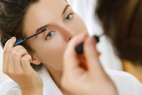Beautiful woman is applying tinted eyebrow gel - Фото, изображение