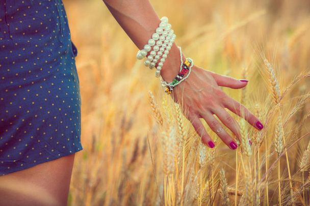 weibliche Hand berührt Ähren der Gerste auf der Wiese bei sonnigem Tag  - Foto, Bild