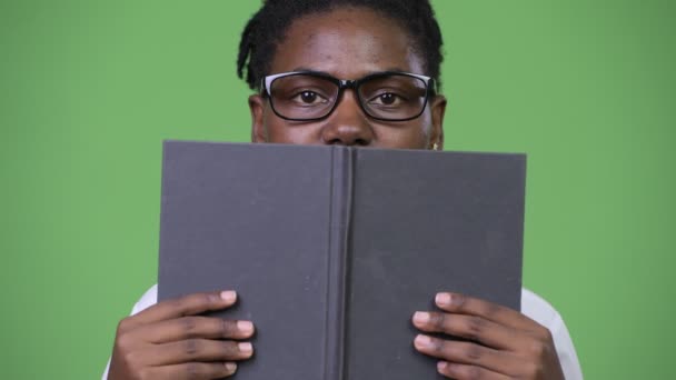 Young beautiful African businesswoman covering face with book - Felvétel, videó