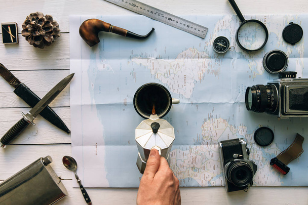 Adventure planning flat lay. Travel vintage gear on map. Man hand in frame pouring coffee from percolator into cup. Exploring lifestyle empty space poster, postcard concept - Zdjęcie, obraz