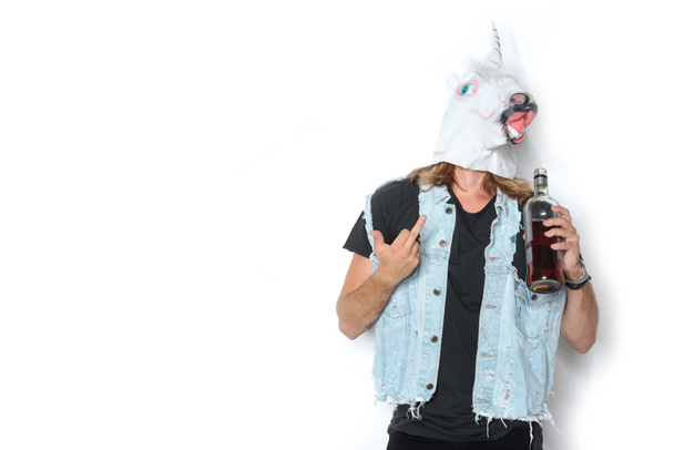 tek boynuzlu at maskesi ve denim yelek şişe rom gösteren orta parmak beyaz adam - Fotoğraf, Görsel