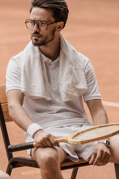 handsome tennis player sitting on chair with tennis racket at court - Photo, Image