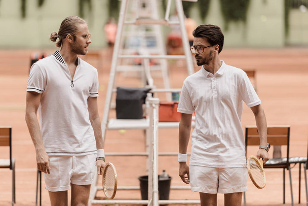 retro tyyliset tennispelaajat kävelevät ja katselevat toisiaan ennen peliä tenniskentällä
 - Valokuva, kuva