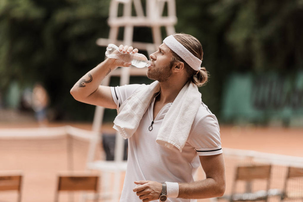 side view of handsome retro styled tennis player drinking water at tennis court - Фото, зображення
