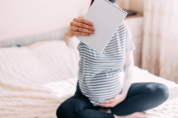 Cheerful pregnant woman making notes in jotter, focuse on paper, belly is unfocused - Photo, image
