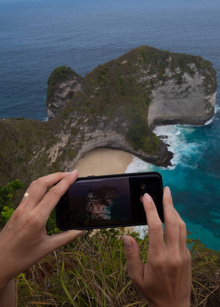 Крупним планом руки з мобільного телефону, робити фото Kelingking пляжу скель в Нуса Пеніда, Балі, Індонезія - Фото, зображення