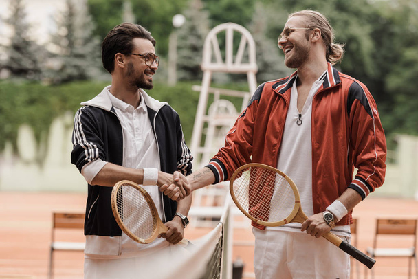 happy retro styled tennis players shaking hands at tennis court - Photo, Image
