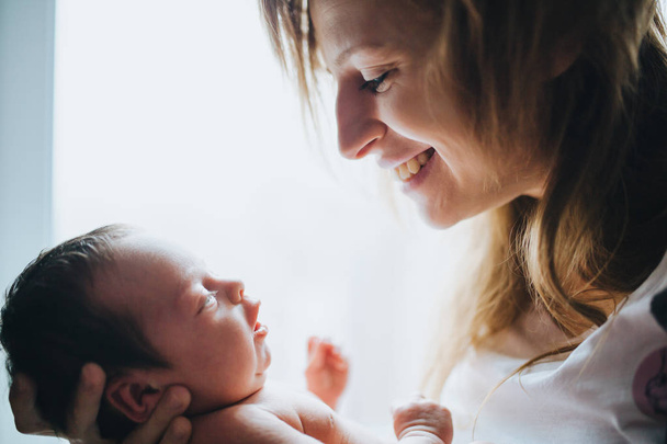 Happy mother holding her small newborn baby. Closeup backlit portrait. - Fotó, kép