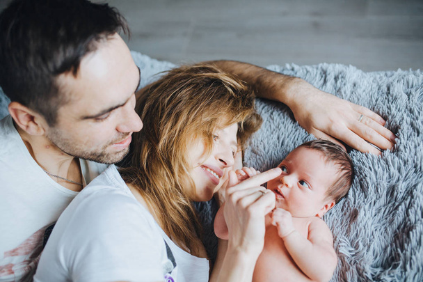 Feliz sorrindo jovem família saudável na cama deitada com a pequena filha recém-nascida. Mãe toca o nariz do bebê
. - Foto, Imagem