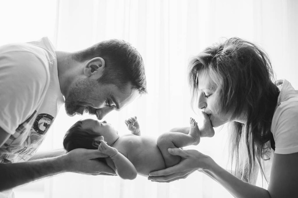 Happy cheerful healthy smiling parents holding naked baby. Backlit black and white picture. - Photo, image