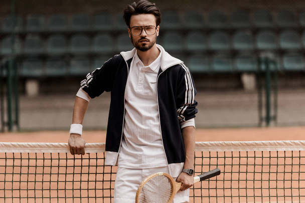 schöner Tennisspieler, der auf dem Tennisplatz in die Kamera schaut und einen Schläger hält - Foto, Bild