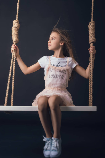 teen girl posing on a swing in Studio on black background in stylish clothes - Φωτογραφία, εικόνα