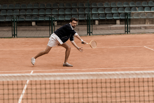 Hübscher Mann im Retro-Stil spielt Tennis mit Schläger auf Tennisplatz - Foto, Bild