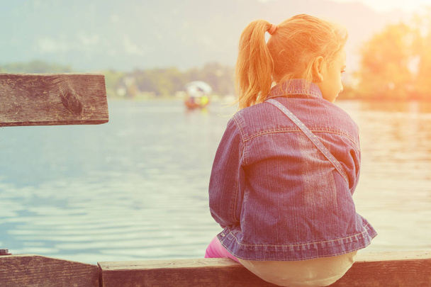 Маленька дівчинка сидить на пірсі біля озера
 - Фото, зображення