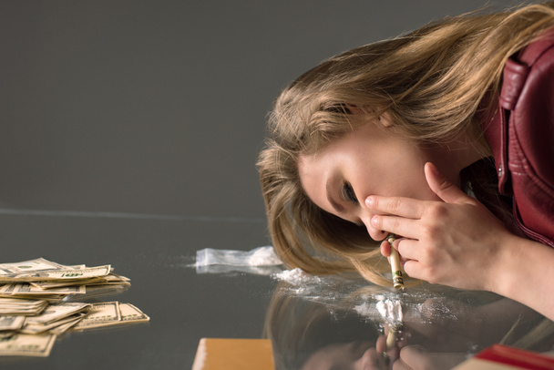 вид збоку залежної молодої жінки, що нюхає кокаїн зі скляного столу
 - Фото, зображення
