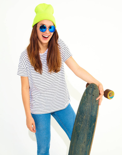 Portrait of young stylish girl model in casual summer clothes in yellow beanie hat posing with longboard desk. Isolated on white - Foto, Imagem