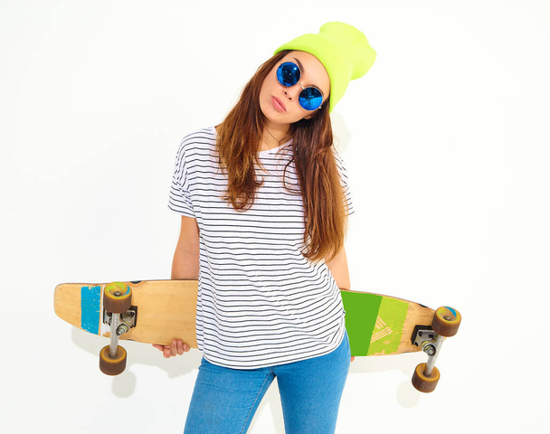 Portrait of young stylish girl model in casual summer clothes in yellow beanie hat posing with longboard desk. Isolated on white - Foto, Imagem