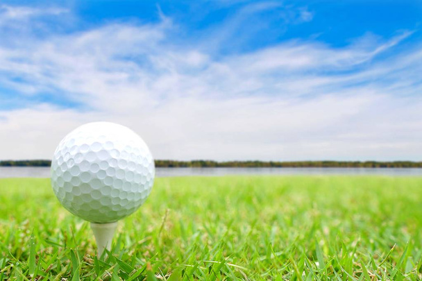 Golf ball on tee in green grass at the beautiful golf course at the ocean side on blue sky and clouds background.Ready to shot.Sport Competition Concept. - Photo, Image