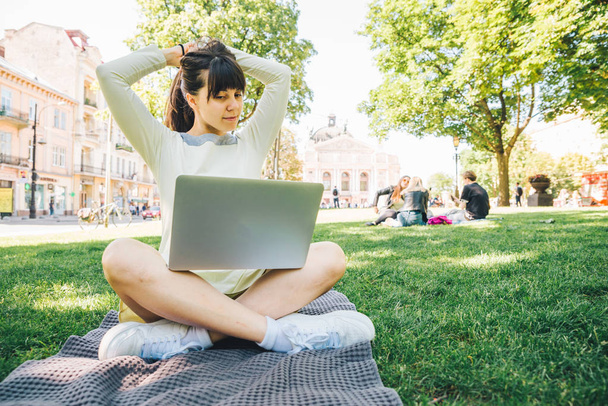 jeune femme adulte pose avec ordinateur portable dans le parc de la ville sur l'herbe verte
 - Photo, image