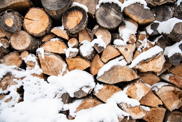 Heap of oak firewood covered with snow, preparation for the winter season, background - Foto, afbeelding